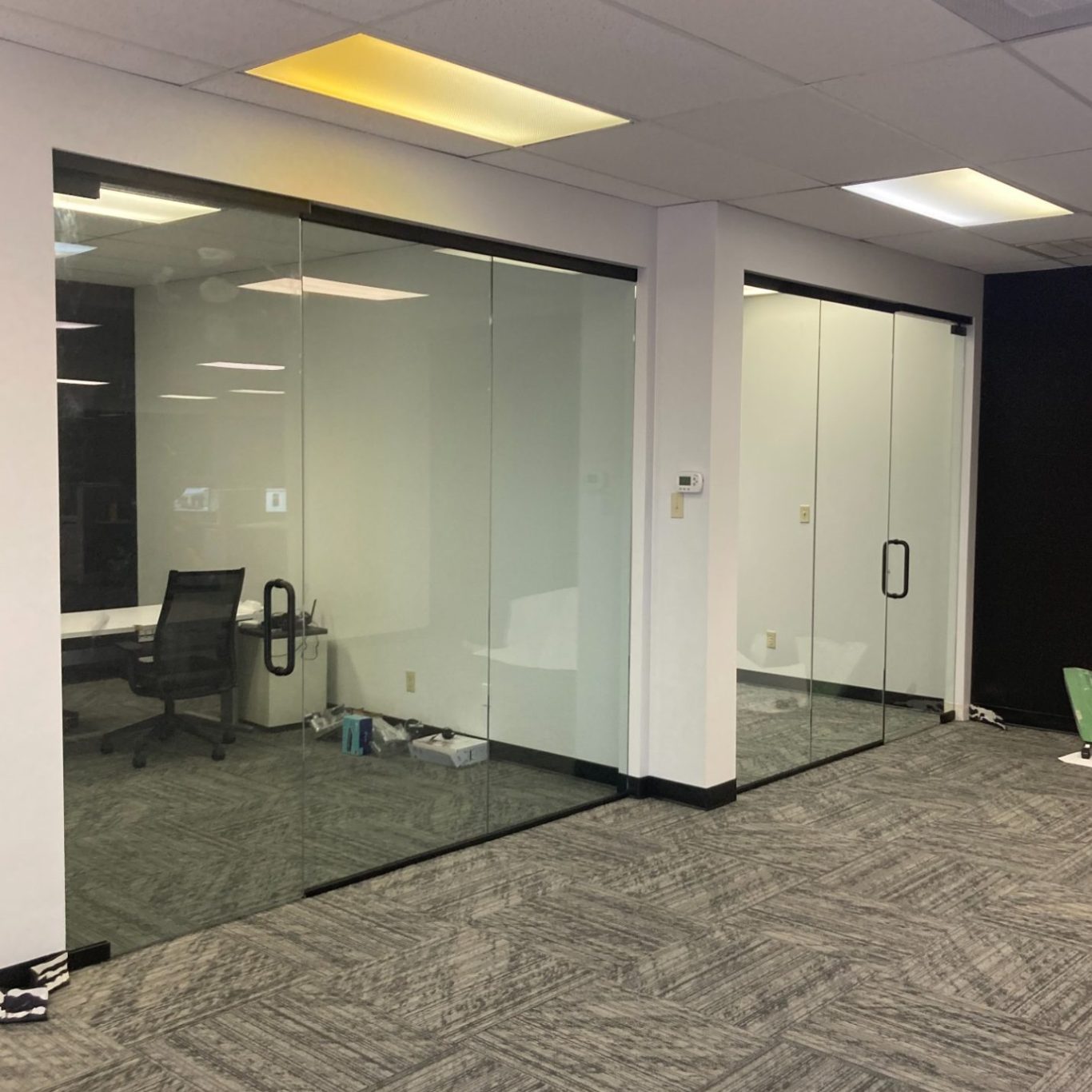 Glass-walled conference rooms with black chairs in an office setting.